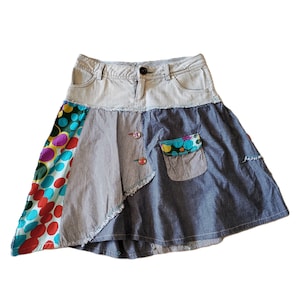 Könnte beinhalten: Ein Patchwork-Rock mit einem hellblauen Jeansbund und Knopfverschluss. Der Rock besteht aus Einsätzen aus blauem Jeansstoff, fein gestreiftem grauem Stoff und einem bunten Bereich mit großen, mehrfarbigen Punkten. Enthält eine aufgesetzte Tasche.