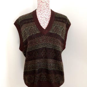 May include: A sleeveless, V-neck sweater vest in shades of brown, burgundy, and olive green. The vest features a geometric pattern across the chest and lower portion. The neckline and armholes are trimmed in a darker burgundy color.