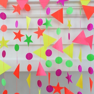 Pode incluir: Uma guirlanda de papel neon com estrelas, círculos e triângulos pendurados em um fundo branco.