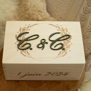 Peut inclure: Une boîte en bois avec un motif floral et les initiales "C. & C." en lettres vertes. La date "1 juin 2024" est inscrite sur le fond de la boîte.
