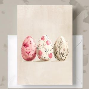 May include: A greeting card featuring three decorative Easter eggs. The eggs are painted with floral designs in shades of pink, white, and brown. The card has a cream-colored background and is accompanied by a white envelope.
