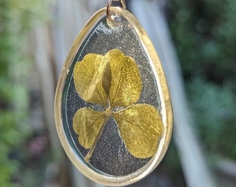 May include: A clear resin keychain with a four-leaf clover pressed inside. The clover is a golden yellow color and is surrounded by a clear resin.