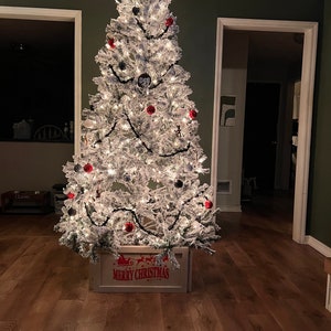 May include: A flocked white Christmas tree with red and black ornaments, a black star on top, and a white wooden box with the words "Merry Christmas" on it.