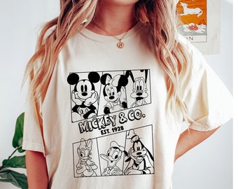 May include: A cream colored t-shirt with a black and white graphic print of Mickey Mouse, Minnie Mouse, Donald Duck, and Goofy. The text on the shirt reads "Mickey & Co. Est. 1928".