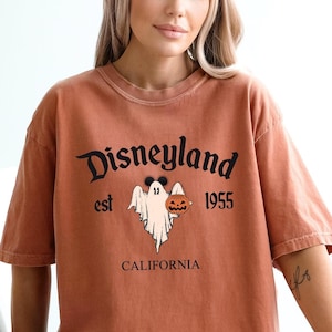 Op de afbeelding: Een verbrand oranje T-shirt met een zwarte afbeelding van een geest die een jack-o-lantern vasthoudt. De afbeelding bevat ook de tekst "Disneyland est 1955 Californi&euml;".