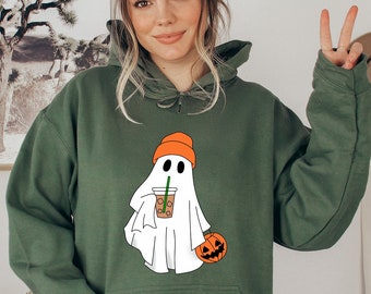 May include: Green hooded sweatshirt with a white ghost wearing an orange hat holding a brown cup with a straw and a small orange pumpkin. The ghost has two black eyes.