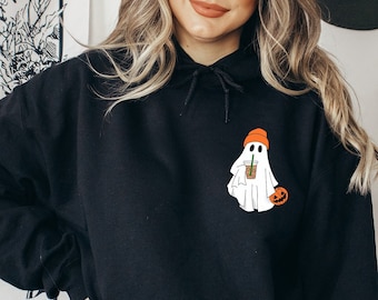 May include: Black hoodie with a white ghost wearing an orange beanie and holding a brown and white cup. The ghost is holding a small orange pumpkin.