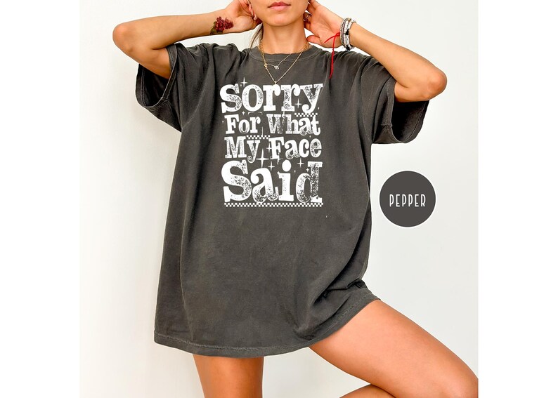 May include: Dark gray oversized t-shirt with the text "Sorry For What My Face Said" in white. The shirt has a vintage, worn look and a round "Pepper" label.