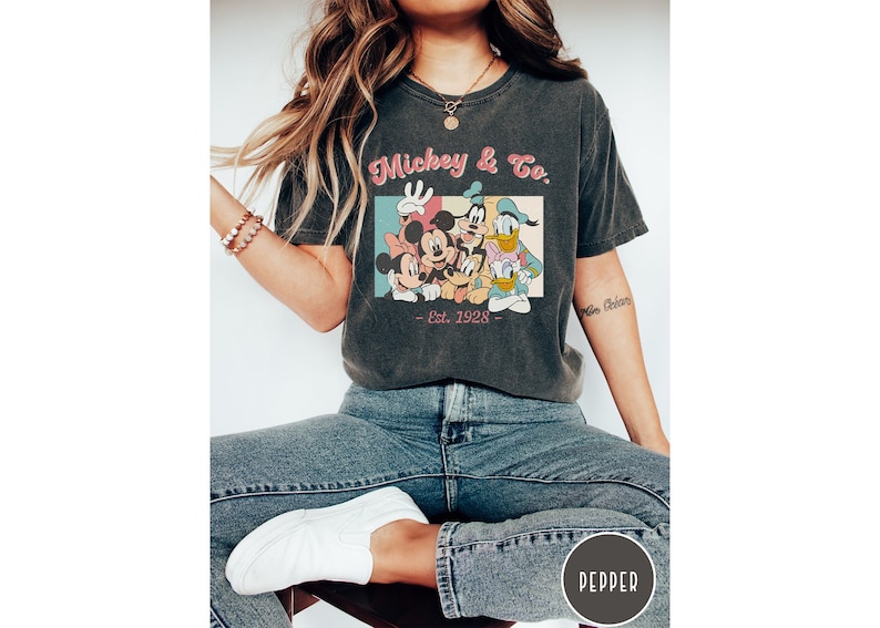 May include: A black t-shirt with a vintage-style graphic of Mickey Mouse and friends. The graphic includes the text "Mickey & Co. - Est. 1928 - ".