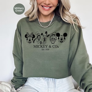 May include: A military green sweatshirt with a black graphic of Mickey Mouse, Minnie Mouse, Goofy, Pluto, Donald Duck, and Mickey Mouse. The text "Mickey & Co." and "Est. 1928" are printed below. A casual style sweatshirt.