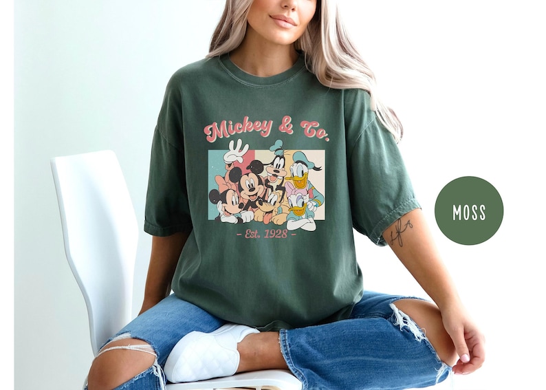 May include: A green t-shirt with a vintage-style graphic of Mickey Mouse and friends. The graphic says "Mickey & Co. - Est. 1928".
