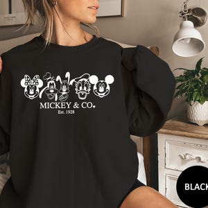May include: Black sweatshirt with white outlines of Mickey Mouse, Minnie Mouse, Donald Duck, Goofy, and Pluto. The text "Mickey & Co. Est. 1928" is printed below the characters. A classic style sweatshirt.