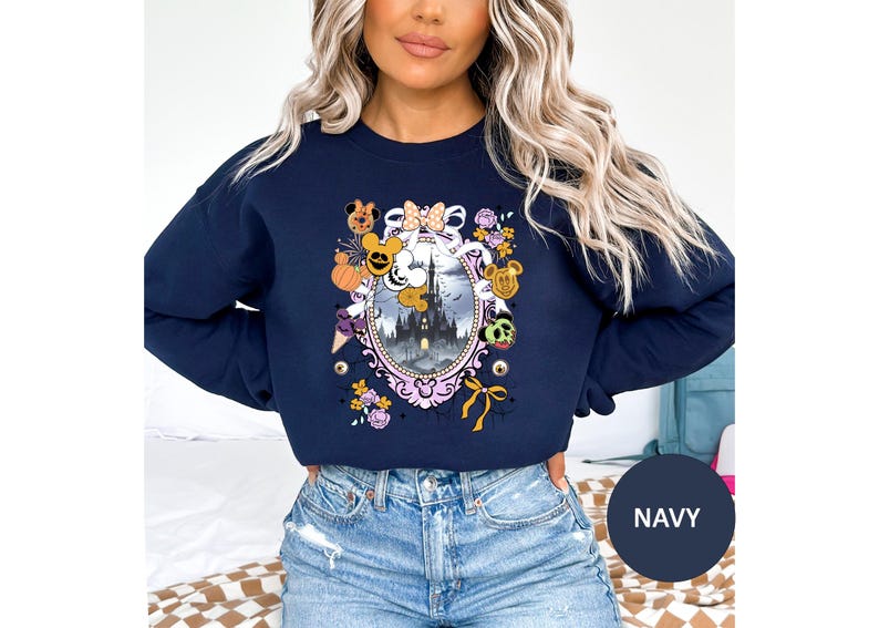 May include: Navy blue sweatshirt featuring a Halloween-themed design. The graphic includes a castle, pumpkins, and character-themed elements within an oval frame. The sweatshirt has a crew neck and long sleeves.