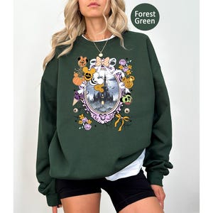 May include: Forest green sweatshirt with a colorful graphic. The graphic features a castle, pumpkins, Mickey Mouse, and other Halloween-themed elements. The sweatshirt is a solid color with a white undershirt peeking out.