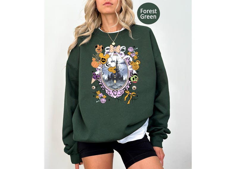 May include: Forest green sweatshirt with a colorful graphic. The graphic features a castle, pumpkins, Mickey Mouse, and other Halloween-themed elements. The sweatshirt is a solid color with a white undershirt peeking out.