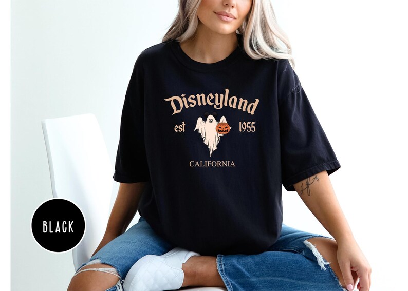 Op de afbeelding: Zwart T-shirt met een grafische print van een geest die een pompoen vasthoudt. De tekst "Disneyland est 1955 Californi&euml;" staat op het T-shirt gedrukt.