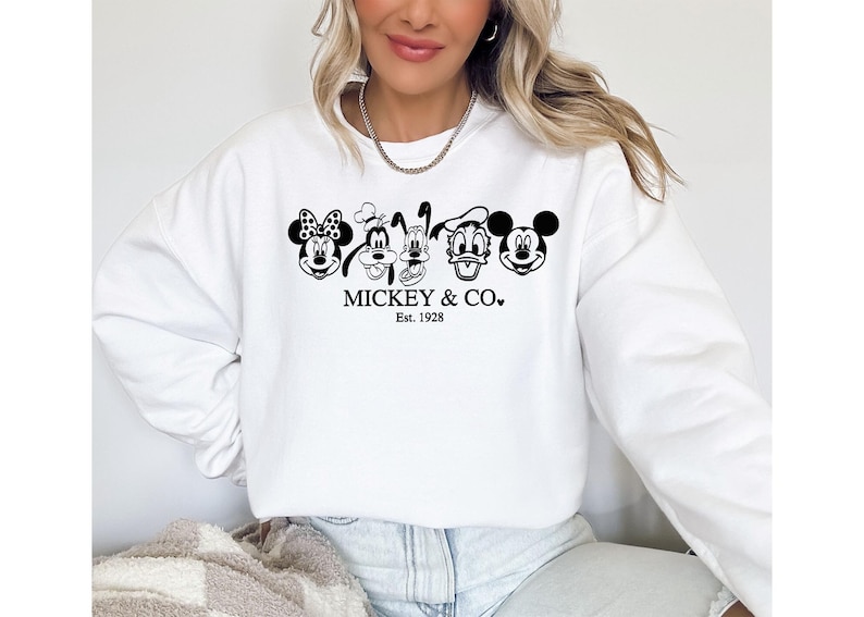 May include: White sweatshirt with a black and white graphic of Mickey Mouse, Minnie Mouse, Goofy, Donald Duck, and Pluto. The text "MICKEY & CO." and "Est. 1928" are printed below the characters. A casual, comfortable style.