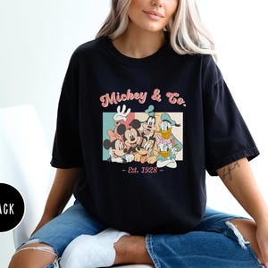 May include: Black t-shirt with a vintage-style graphic of Mickey Mouse, Minnie Mouse, Donald Duck, Goofy, and Pluto. The graphic includes the text "Mickey & Co. - Est. 1928 - "