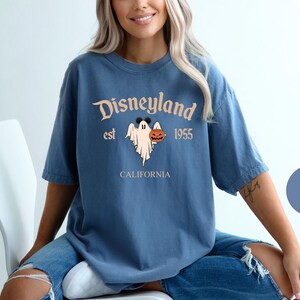 Op de afbeelding: Een blauw T-shirt met een vintage Disneyland-afbeelding met een spook dat een pompoen vasthoudt. De tekst luidt "Disneyland est 1955 Californi&euml;".