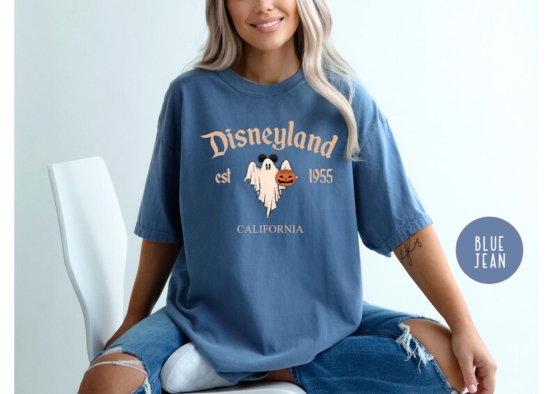 Op de afbeelding: Een blauw T-shirt met een vintage Disneyland-afbeelding met een spook dat een pompoen vasthoudt. De tekst luidt "Disneyland est 1955 Californi&euml;".