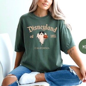 Op de afbeelding: Een groen T-shirt met een vintage-stijl afbeelding van een geest die een pompoen vasthoudt. De tekst op het shirt luidt "Disneyland est 1955 Californi&euml;".