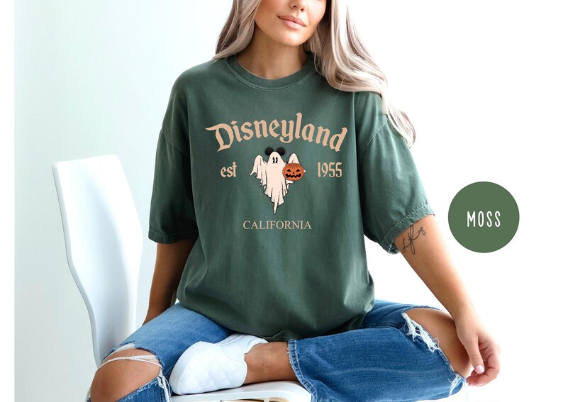 Op de afbeelding: Een groen T-shirt met een vintage-stijl afbeelding van een geest die een pompoen vasthoudt. De tekst op het shirt luidt "Disneyland est 1955 Californi&euml;".