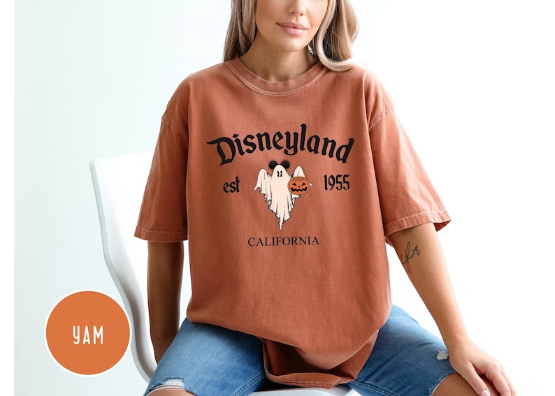 Op de afbeelding: Een verbrand oranje T-shirt met een zwarte afbeelding van een geest die een jack-o-lantern vasthoudt. De afbeelding bevat ook de tekst "Disneyland est 1955 Californi&euml;".