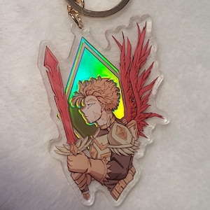 May include: A clear acrylic keychain featuring a character illustration with red wings and a sword. The keychain has a gold-colored clasp and a gold-colored ring. The character has blonde hair and is wearing armor. The text "EAS SALART" is visible.