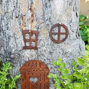May include: Rustic metal fairy house decor with a heart-shaped door, window, and circle design. The house is attached to a tree trunk.