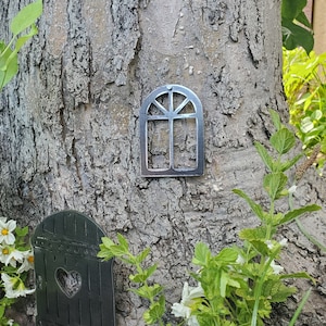 May include: A metal window cutout with a heart-shaped opening, attached to a tree trunk. The window is silver and has a rustic look.