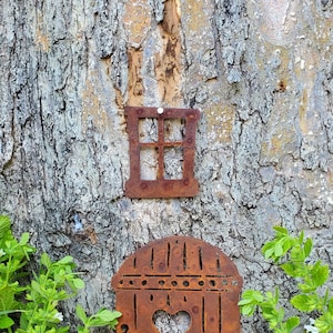 May include: A rusty metal birdhouse with a heart-shaped opening and a window with a grid pattern attached to a tree trunk.