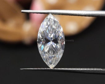 May include: A marquise-cut diamond held by tweezers against a black background. The diamond is clear and faceted, reflecting light. The tweezers are silver. In the blurred background, there is a pink and brown object.