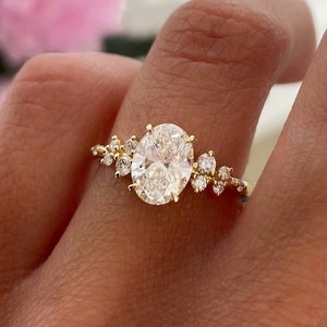 May include: A gold engagement ring with an oval-shaped center diamond and smaller diamonds set around it.