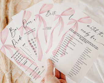 Könnte beinhalten: Vier rosa und weiße Babyparty-Spielkarten mit rosa Schleifen. Die Karten sind mit "Baby-Vorhersagen", "Über oder Unter", "Süßigkeiten-Bar-Spiel" und "Brite Hatch Eat Counterpart" betitelt.