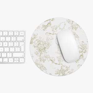 May include: A white round mouse pad with a beige pattern of animals and trees. A white computer mouse is on top of the mouse pad.