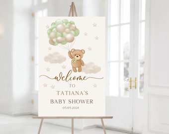 May include: Welcome to Tatiana's Baby Shower sign with a brown teddy bear holding green and beige balloons, clouds, and stars on a beige background.
