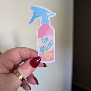 May include: A sticker depicting a pink spray bottle with a blue nozzle. The sticker features the words "TERF REPELLENT" in white, and a yellow starburst that reads "100% EFFECTIVE GUARANTEE".