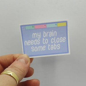 May include: A blue and white sticker with the text "my brain needs to close some tabs". The sticker is designed to look like a computer window with a close button, a star, a heart, and a music note.