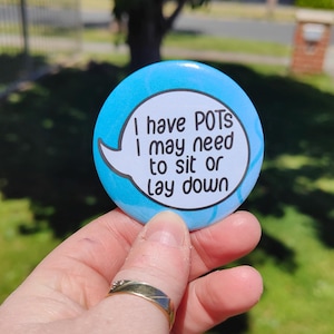 May include: A blue button with a white speech bubble that reads "I have POTS I may need to sit or lay down".