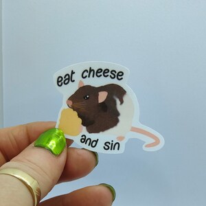 Op de afbeelding: Witte sticker met een cartoonrat met bruin en wit haar die kaas eet. De sticker heeft de tekst "eat cheese and sin" in zwarte letters.