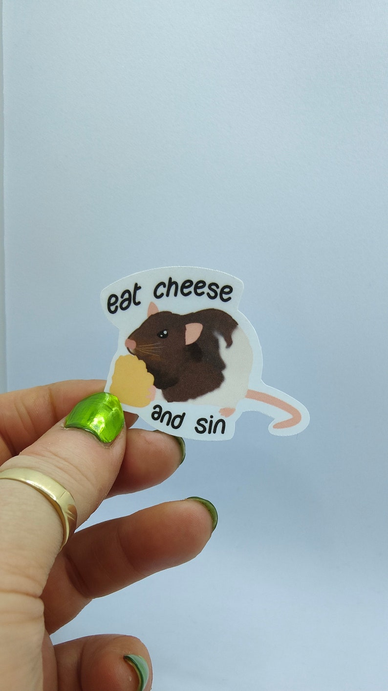 Op de afbeelding: Witte sticker met een cartoonrat met bruin en wit haar die kaas eet. De sticker heeft de tekst "eat cheese and sin" in zwarte letters.
