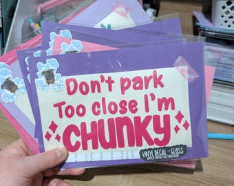 Op de afbeelding: Een rechthoekige vinyl sticker in een doorzichtige beschermhoes met de roze tekst Don't park Too close I'm CHUNKY en vier kleine roze sterren. Een kleine sticker van een mopshond omringd door blauwe bubbels bevindt zich in de linkerbovenhoek.