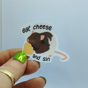 Op de afbeelding: Een sticker met een cartoonrat met bruin en wit haar, die kaas eet. De sticker heeft de tekst "eat cheese and sin" in een zwarte, vette letter.
