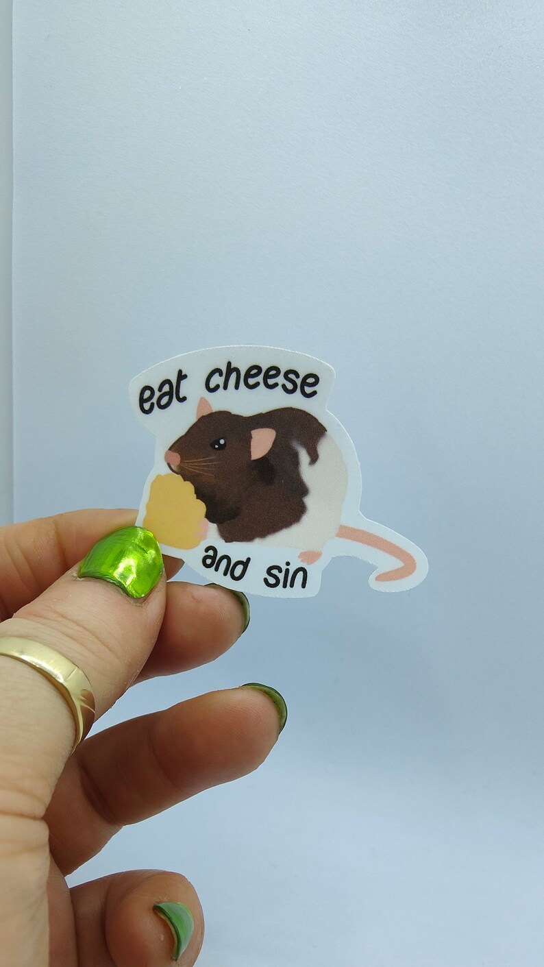 Op de afbeelding: Een sticker met een cartoonrat met bruin en wit haar, die kaas eet. De sticker heeft de tekst "eat cheese and sin" in een zwarte, vette letter.