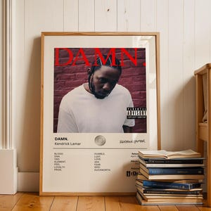 Könnte beinhalten: Ein Poster für das Album "DAMN." von Kendrick Lamar. Das Poster zeigt einen roten Backsteinwandhintergrund mit einem Porträt von Kendrick Lamar in der Mitte. Der Albumtitel ist in großen roten Buchstaben oben auf dem Poster. Die Tracklist des Albums ist unten auf dem Poster aufgelistet.