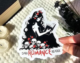 May include: A white sticker with a black silhouette of a woman reading a book. She is surrounded by skulls and red roses. The text "DARK ROMANCE READER" is written in red at the bottom of the sticker.