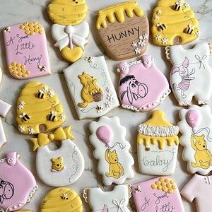 May include: A set of Winnie the Pooh themed sugar cookies decorated with yellow, pink, and white icing. The cookies feature Winnie the Pooh, Piglet, Eeyore, and a honey pot. The cookies are perfect for a baby shower or birthday party.