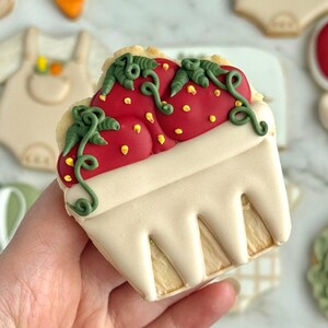 Farmers market-themed baby shower sugar cookies featuring hand-decorated designs like “little sprout,” baby onesies with vegetables, carrots, corn, strawberries, tomatoes, baby bottles, mason jars, leafy greens, and baby mobiles. Adorned with soft green, beige, orange, and red royal icing, these custom cookies are perfect for a “locally grown” or garden baby shower theme, gender-neutral celebrations, and personalized baby gifts.