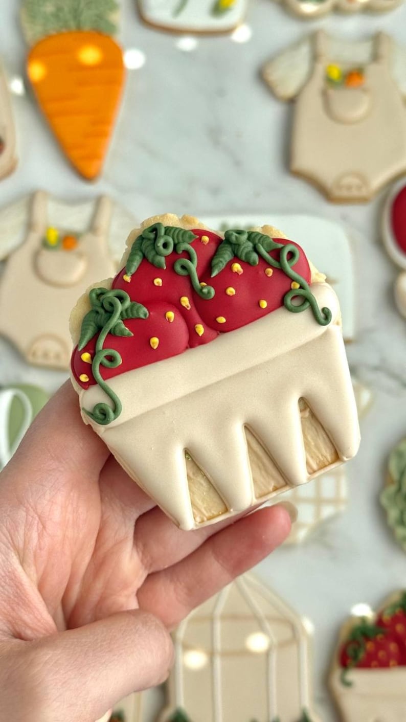 Farmers market-themed baby shower sugar cookies featuring hand-decorated designs like “little sprout,” baby onesies with vegetables, carrots, corn, strawberries, tomatoes, baby bottles, mason jars, leafy greens, and baby mobiles. Adorned with soft green, beige, orange, and red royal icing, these custom cookies are perfect for a “locally grown” or garden baby shower theme, gender-neutral celebrations, and personalized baby gifts.