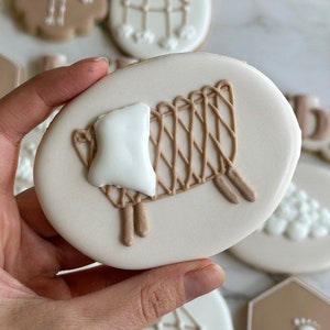 May include: A collection of decorated sugar cookies with various baby-themed designs, including a crib, a mobile, a stork, and footprints. The cookies are decorated with white and brown icing.